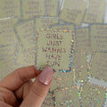 Holographic 'GIRLS JUST WANNA HAVE FUN' sticker held by a hand with pink nail polish against a background of similar stickers.